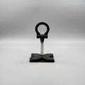A black metal stand with a circular top loop and a square base, shown on a white tabletop with shipping boxes partially visible in the background.